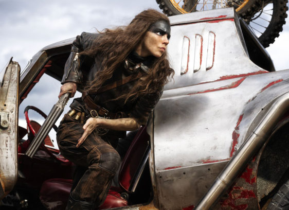 Woman with paint on her face, holding a gun, stands by some sort of vehicle