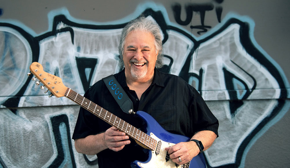 Man holding a guitar in front of a wall with graffiti