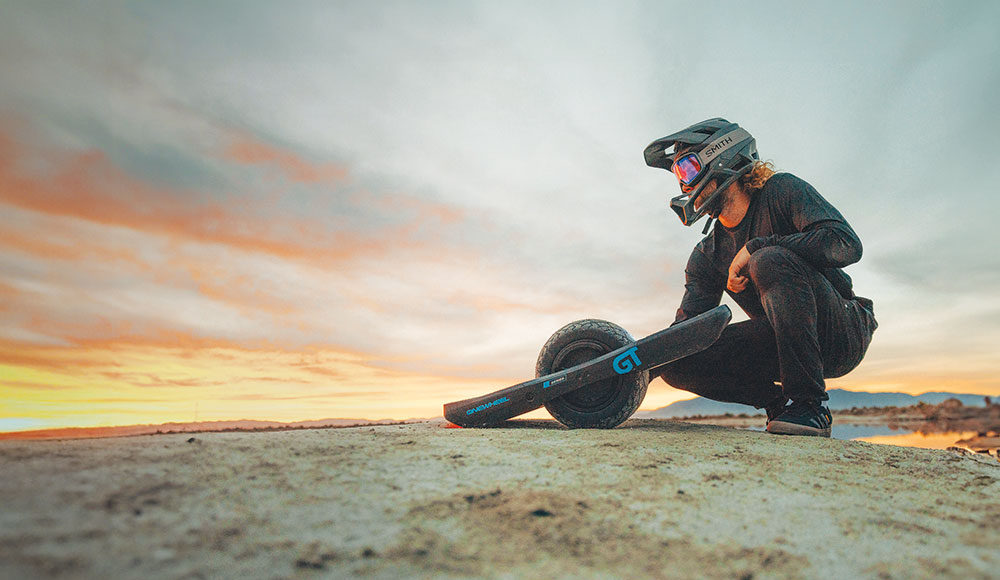 Onewheel rider kneeling down and looking at a beautiful sunset