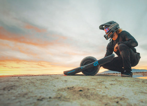 Onewheel rider kneeling down and looking at a beautiful sunset