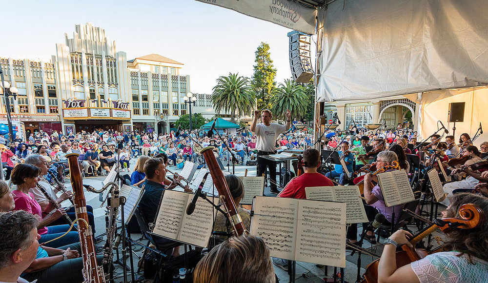 Orchestra playing outdoors in front of a large crowd