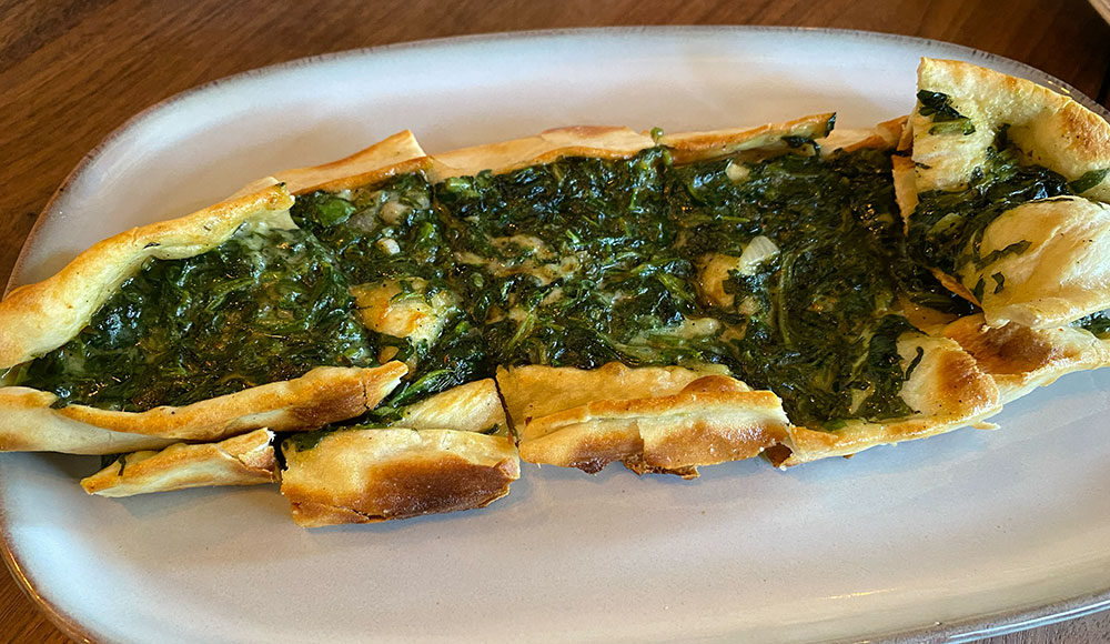 An oval bread with spinach and cheese on top