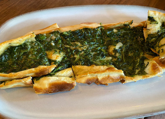 An oval bread with spinach and cheese on top