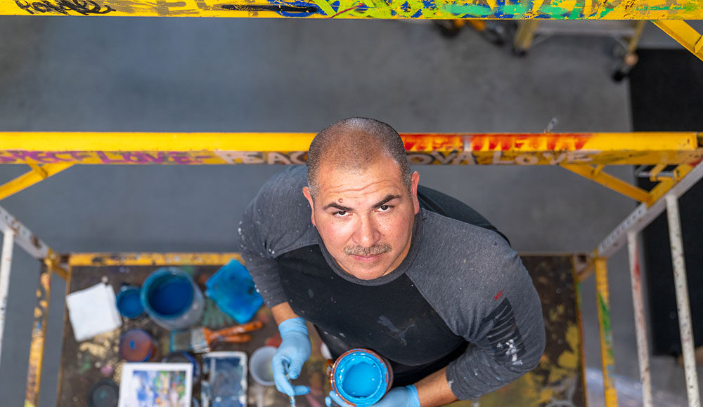 Man on a scaffold holding paint and a brush