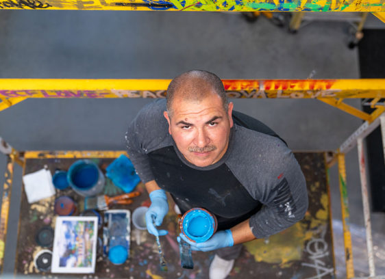 Man on a scaffold holding paint and a brush