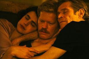 Three actors holding each other closely, appearing to be in bed