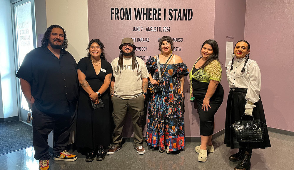 Six people in a gallery in front of a sign that says 