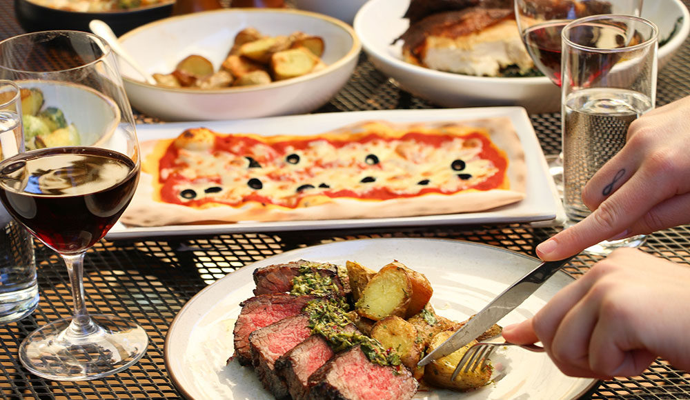 Four dishes on a table, including steak and potatoes and pizza