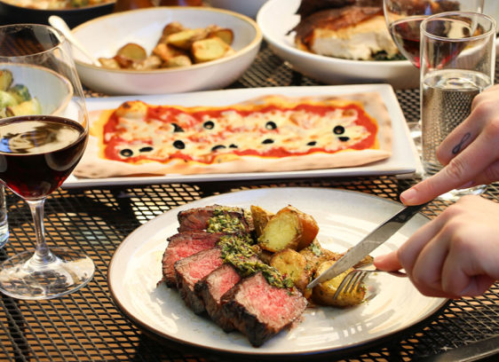 Four dishes on a table, including steak and potatoes and pizza