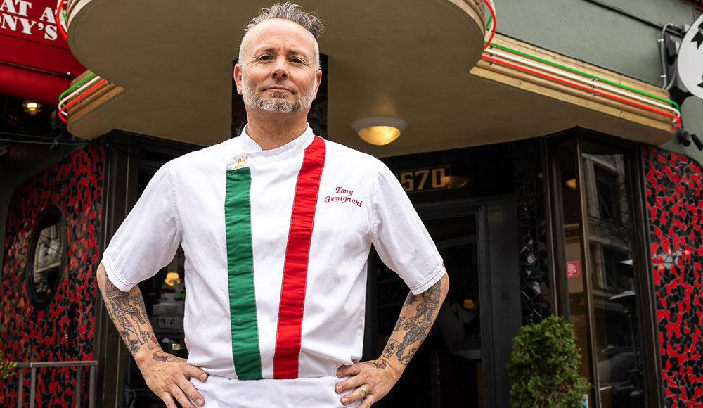 Restaurateur standing in front of one of his restaurants wearing an apron with the colors of the Italian flag