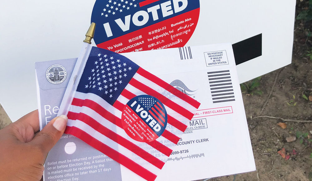 Hand holding a flag, an “I Voted” sticker and a ballot