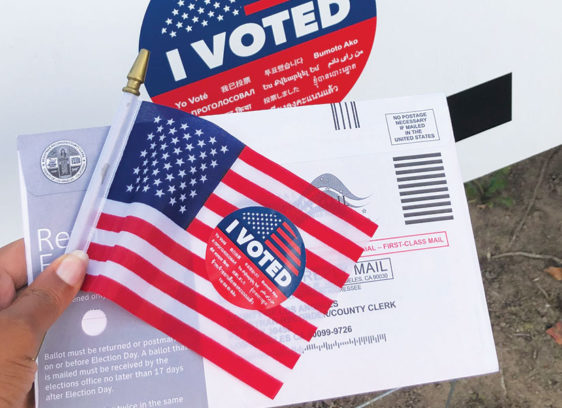 Hand holding a flag, an “I Voted” sticker and a ballot
