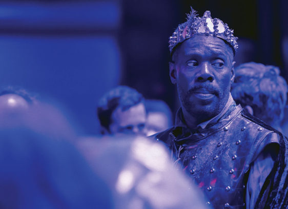 Man wearing a crown, shown in moody stage lighting