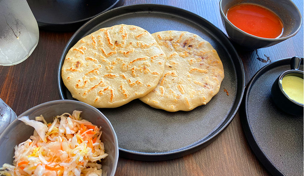 Two pupusas on a plate with bowls of cabbage and red salsa on the side