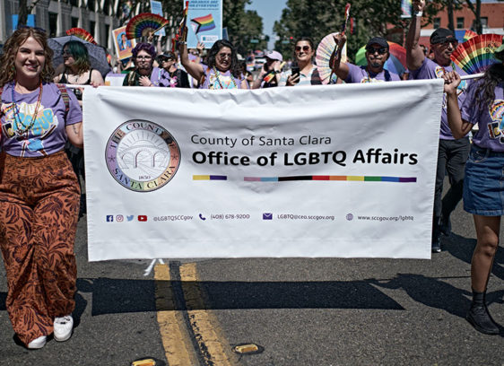 Parade with members of the Santa Clara County Office of LGBTQ Affairs marching with a banner