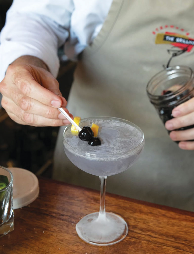 Man wearing an apron putting a luxardo cherry garnish into a drink