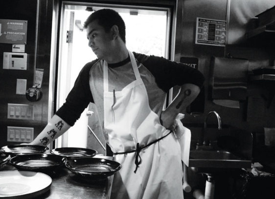 Black-and-white photo of man in a kitchen wearing an apron