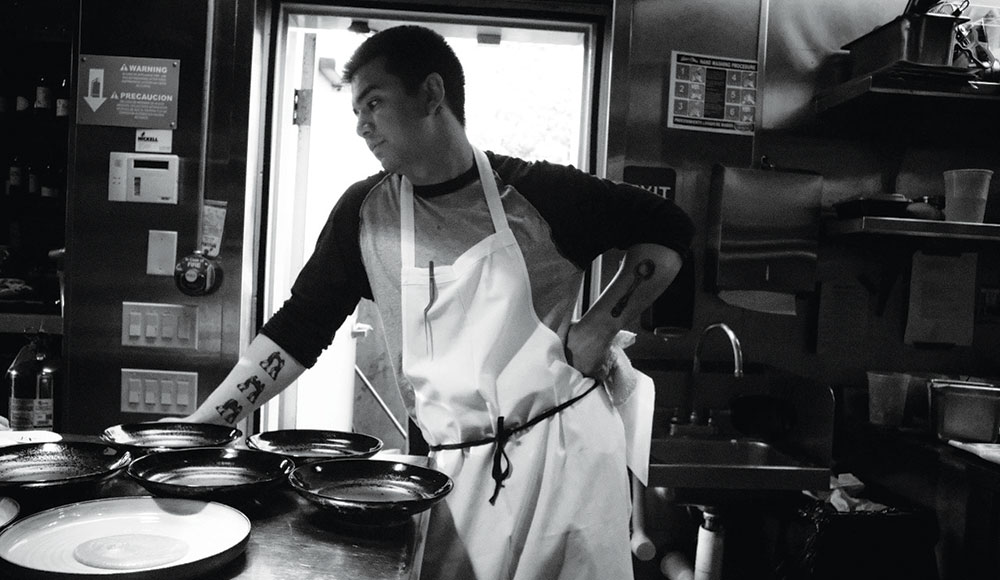 Black-and-white photo of man in a kitchen wearing an apron