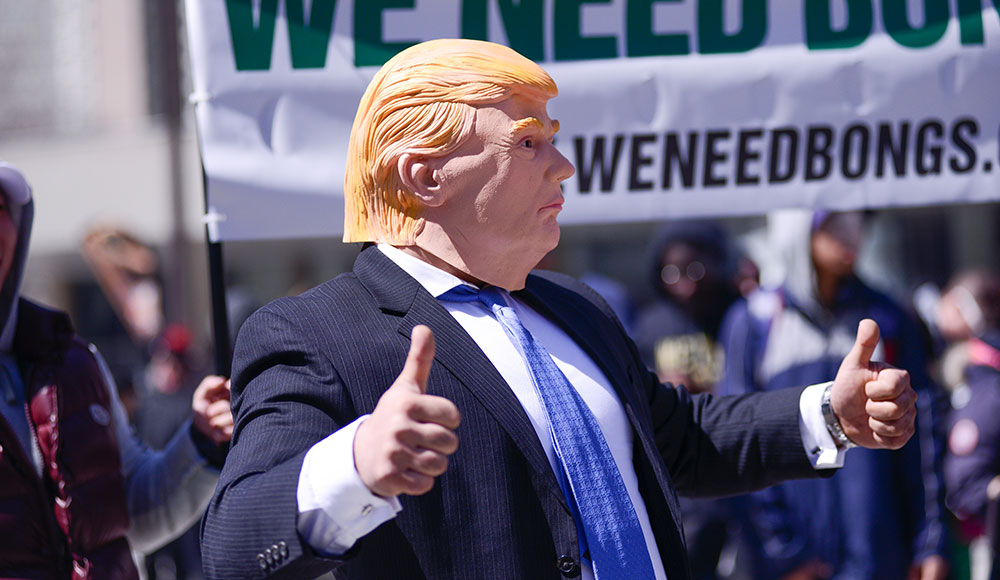 Man dressed in a suit wearing a Donald Trump mask at a rally