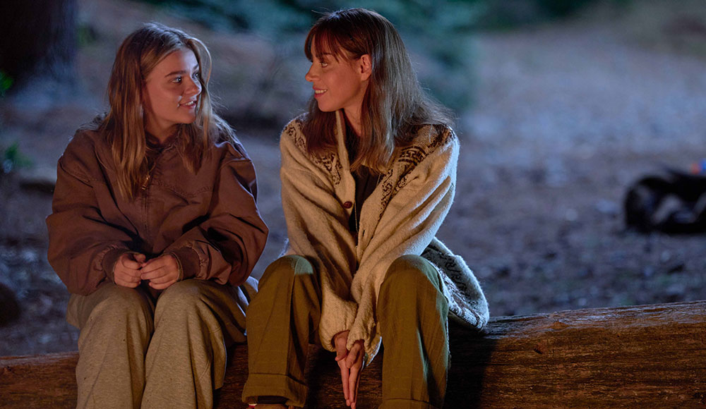 Two women sitting outside on a log