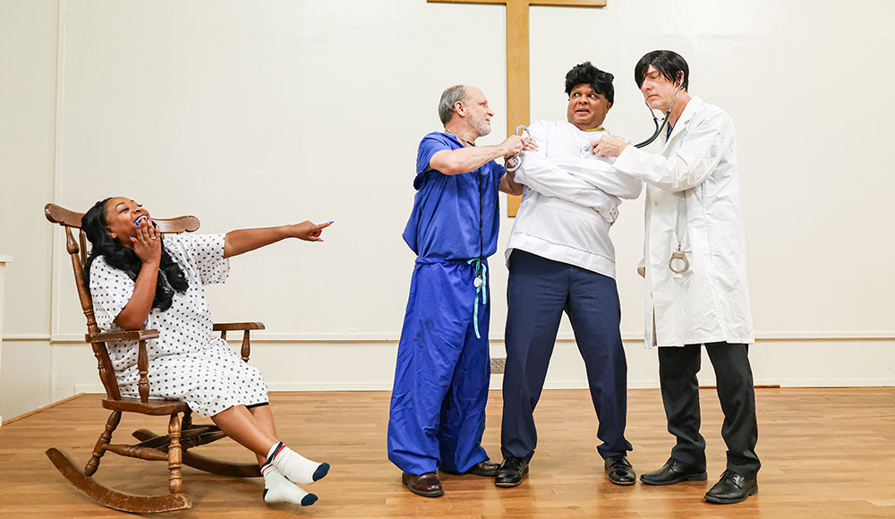 Four actors in a scene set in an insane asylum with one man in a straitjacket