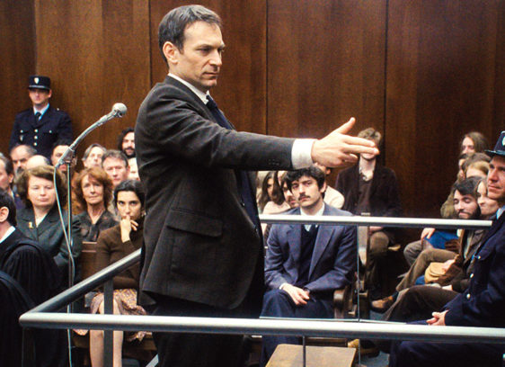 Man holding his hand like a gun and pointing at others in a courtroom