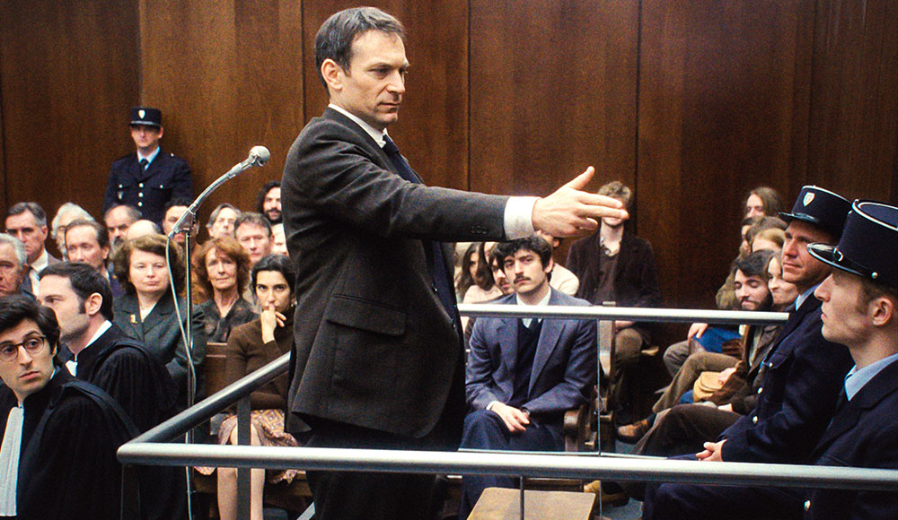 Man holding his hand like a gun and pointing at others in a courtroom