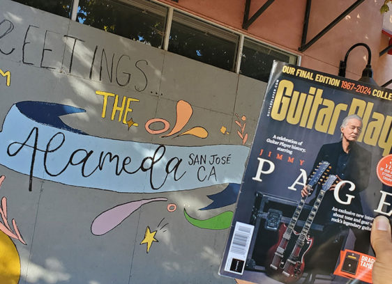 Hand holding up a magazine in front of a boarded-up building