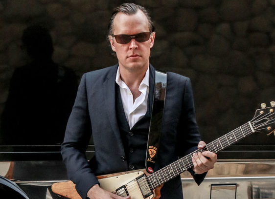 Man holding a guitar, wearing sunglasses