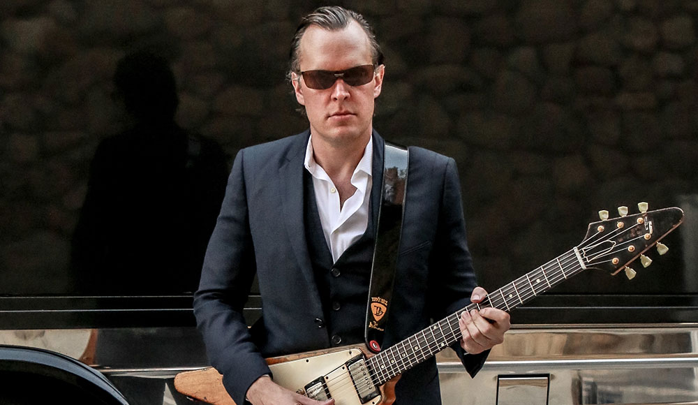 Man holding a guitar, wearing sunglasses