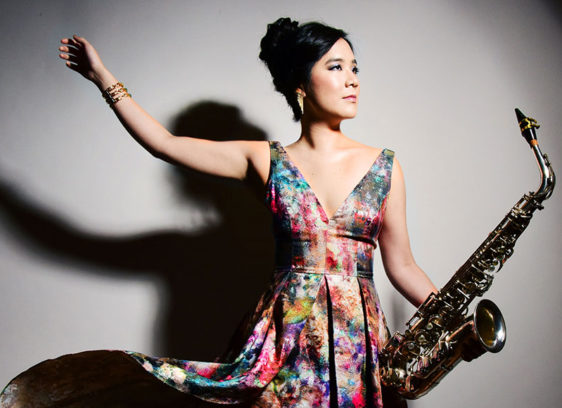 Woman in a flowing flowered dress holding a saxophone