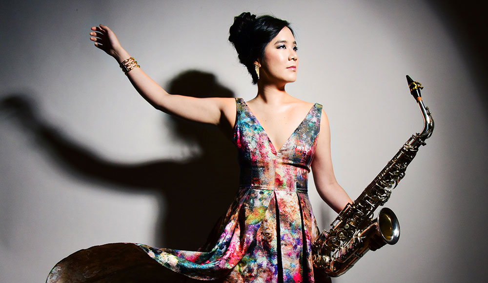 Woman in a flowing flowered dress holding a saxophone