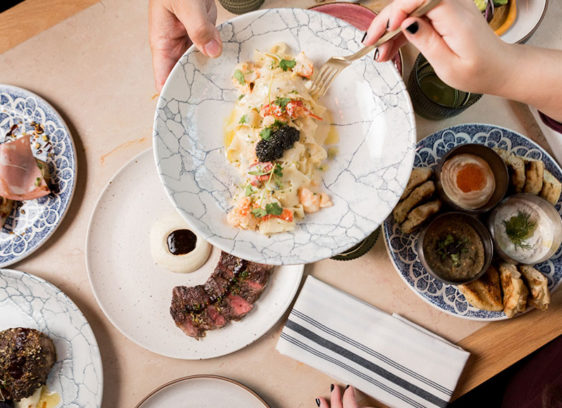 Multiple dishes on a table with hands serving food