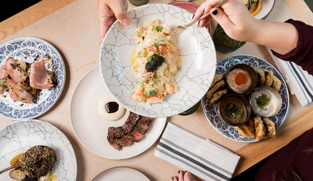 Multiple dishes on a table with hands serving food