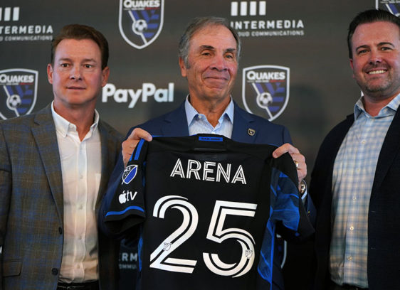 Man holding up a team shirt with the number 25, flanked by two other men