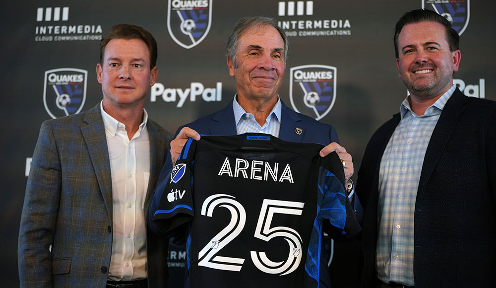 Man holding up a team shirt with the number 25, flanked by two other men