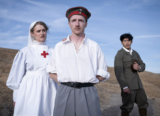 A woman dressed as a Red Cross nurse and two men dressed as World War II soldiers stand in a field