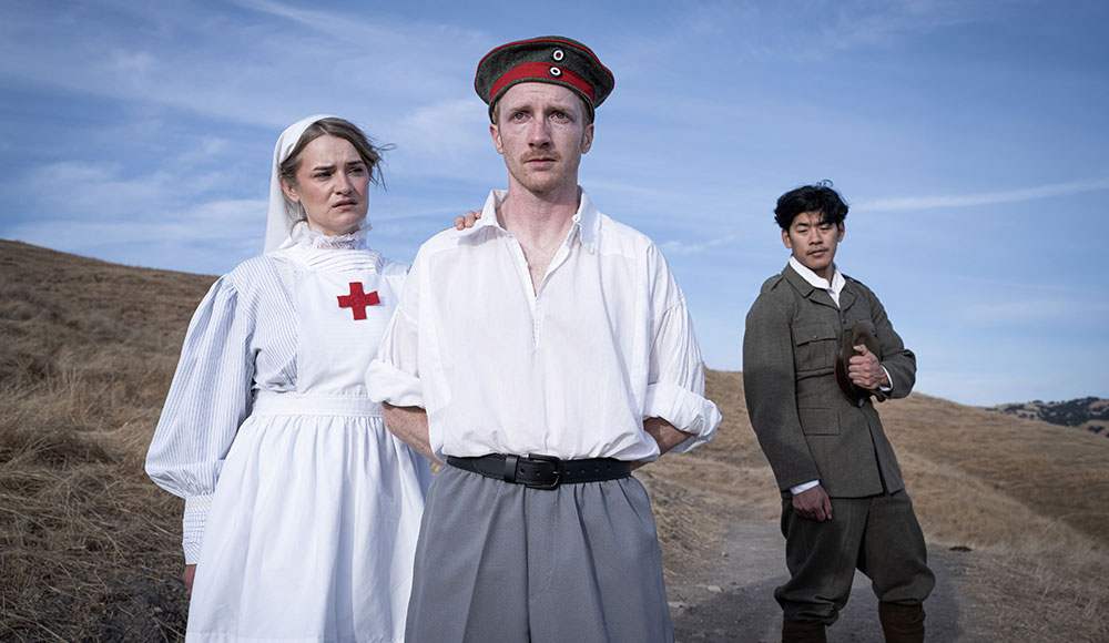 A woman dressed as a Red Cross nurse and two men dressed as World War II soldiers stand in a field