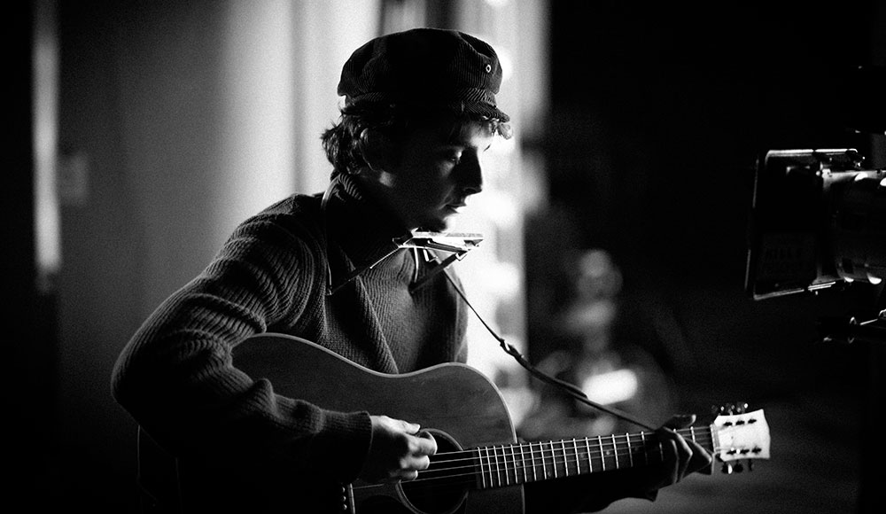 Black and white photo of man playing a guitar, wearing a hat