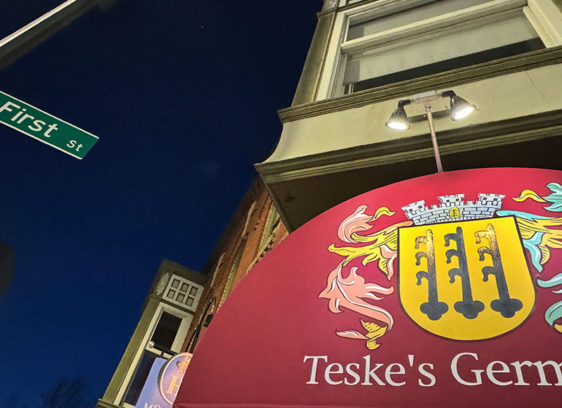 Restaurant sign lit up at dust, shot from below with a street sign in the frame