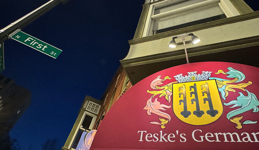 Restaurant sign lit up at dust, shot from below with a street sign in the frame