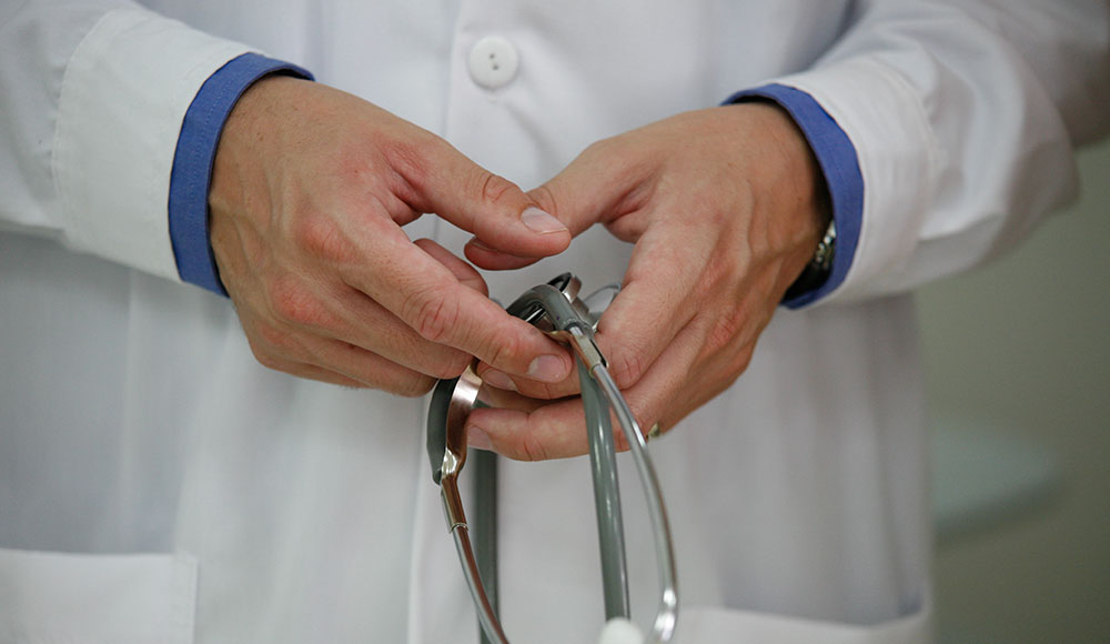 Hands holding stethoscope in front of a white coat