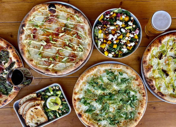 several pizzas and side dishes on a table