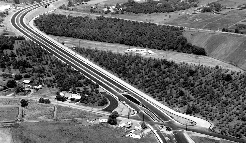 Aerial view of a highway traversing agricultural land, with new development sprouting up