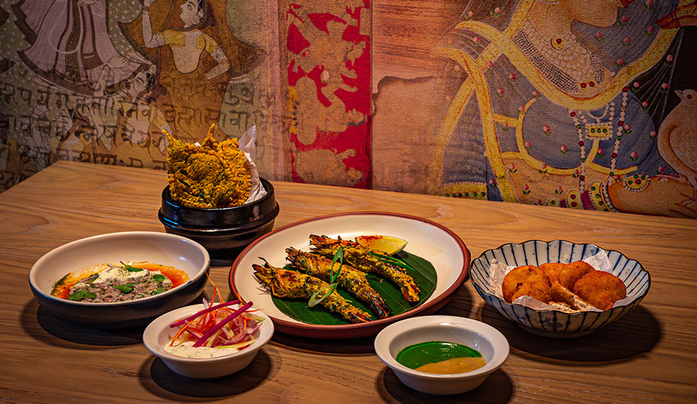 Six plates of food on a table with a colorful wall in the background