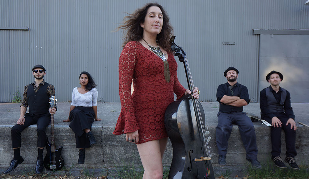 Woman holding a cello in front of four other bandmates